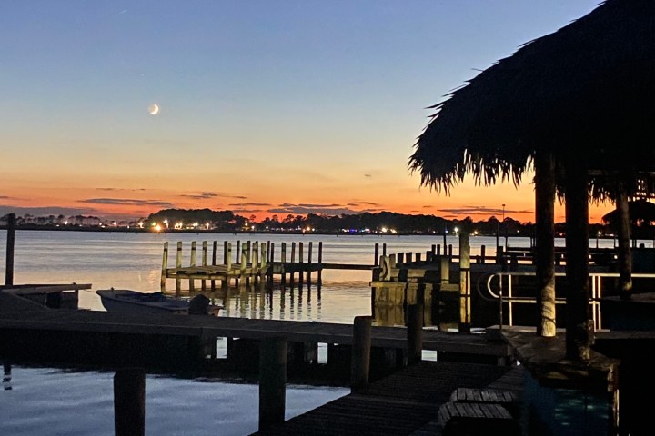 Twilight over a calm lake with docks and a thatched roof structure.