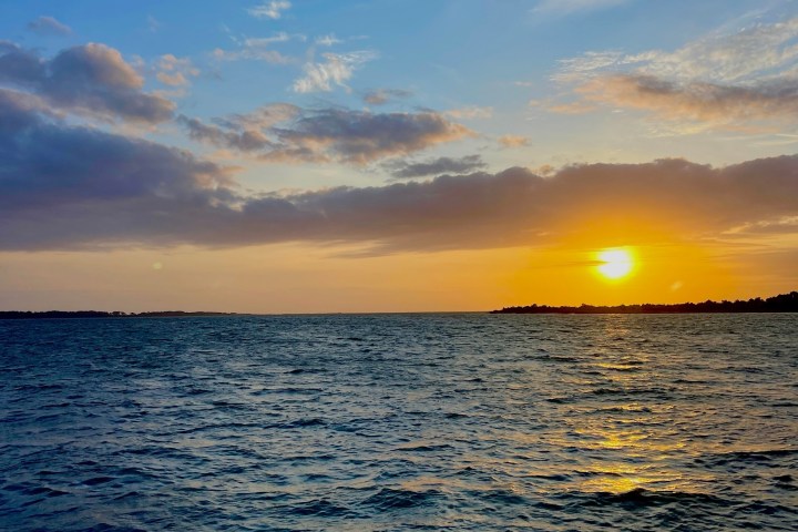 Sunset over a calm ocean with clouds in a blue sky.