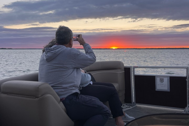 Person on boat photographing a sunset over calm water.
