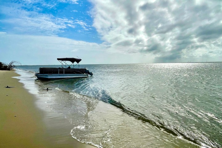 Boat on sandy beach with waves and cloudy sky.
