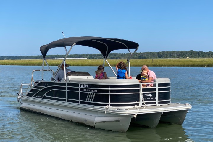 People on a pontoon boat in a calm river with clear sky.