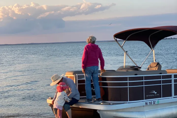Child and adult near pontoon boat on a sandy beach at sunset.