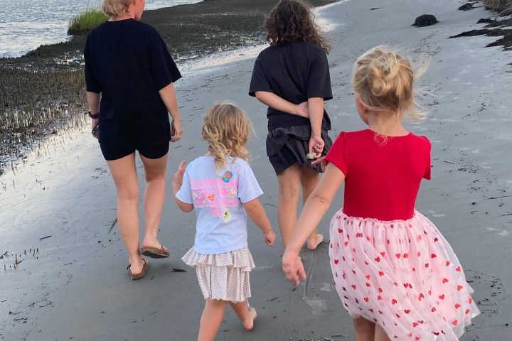 Four people walking on a beach at sunset, wearing casual clothes.