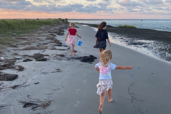 Three children running on a sandy beach at sunset.