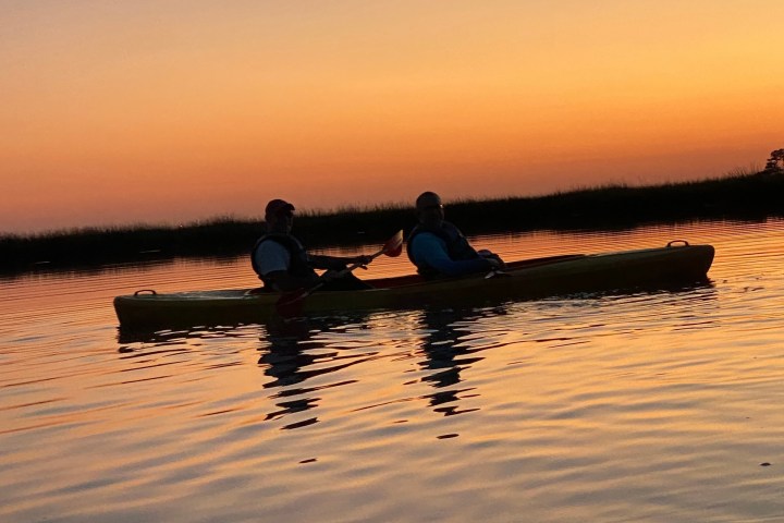 Two people kayaking on calm water at sunset.
