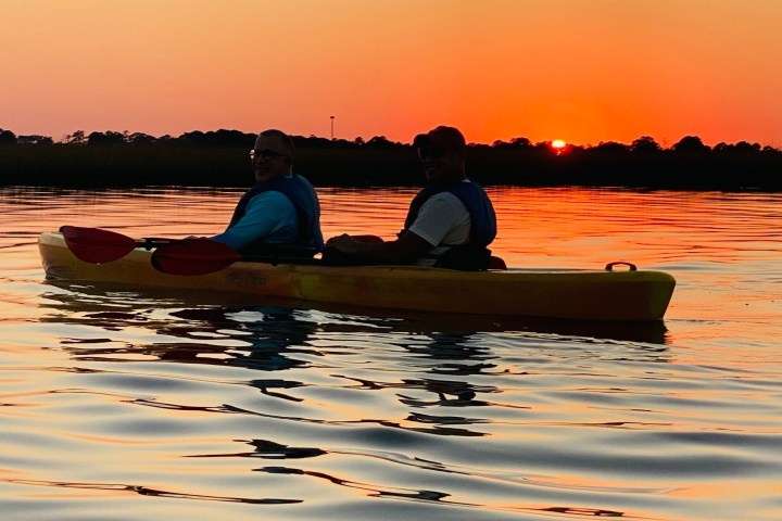 Two people kayaking on a lake at sunset.