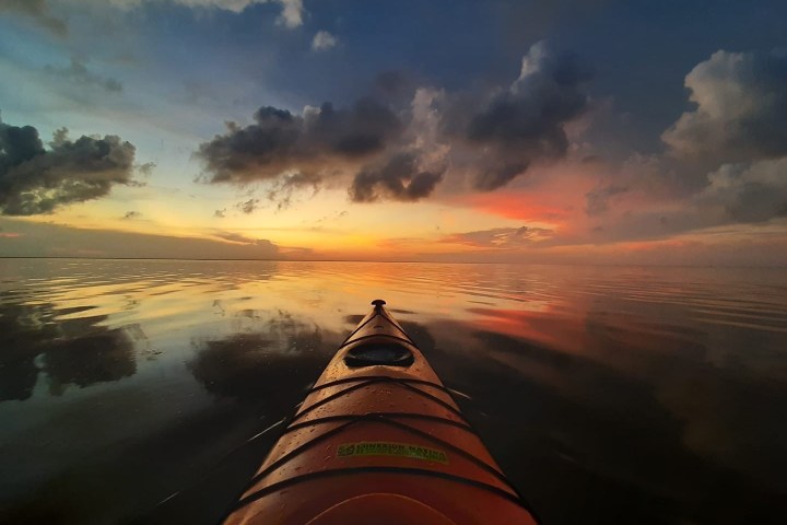 Kayak on calm water during sunset with colorful sky and clouds.